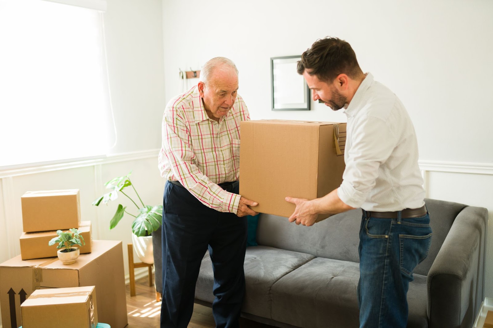 A young man helps his senior father move a box as they start the move to a new senior community.