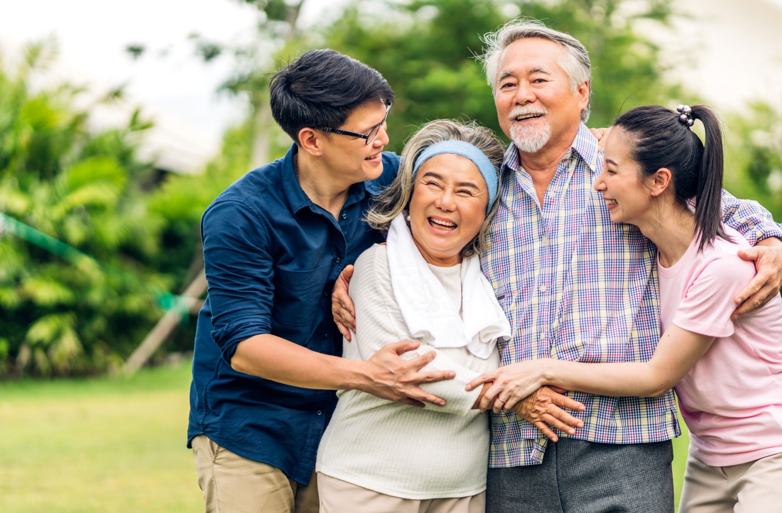A smiling family of 2 adult children and their aging parents enjoy a day outside together.