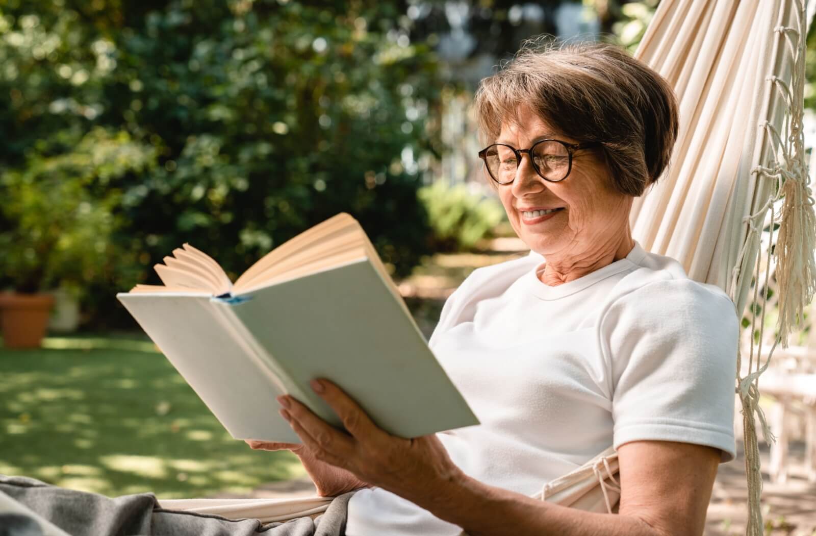 A happy senior enjoys an afternoon outside reading their favorite book.