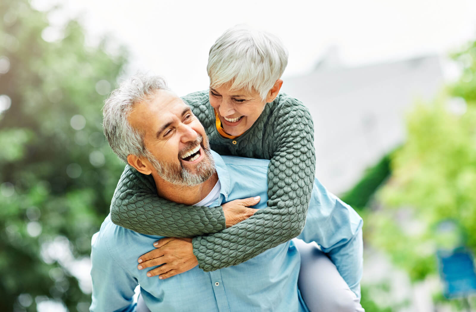 An older couple having a piggyback ride in the park while laughing in the summer.