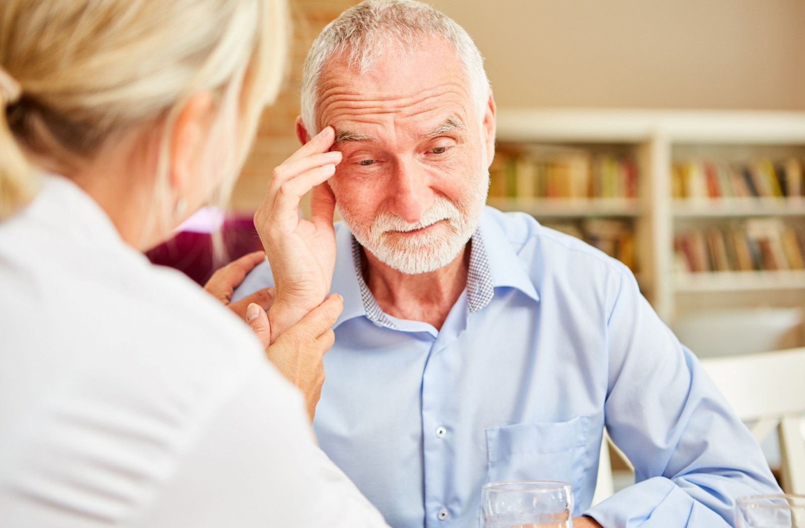 An older adult with Lewy body dementia touches their forehead in concern after receiving a diagnosis during a healthcare checkup with their doctor