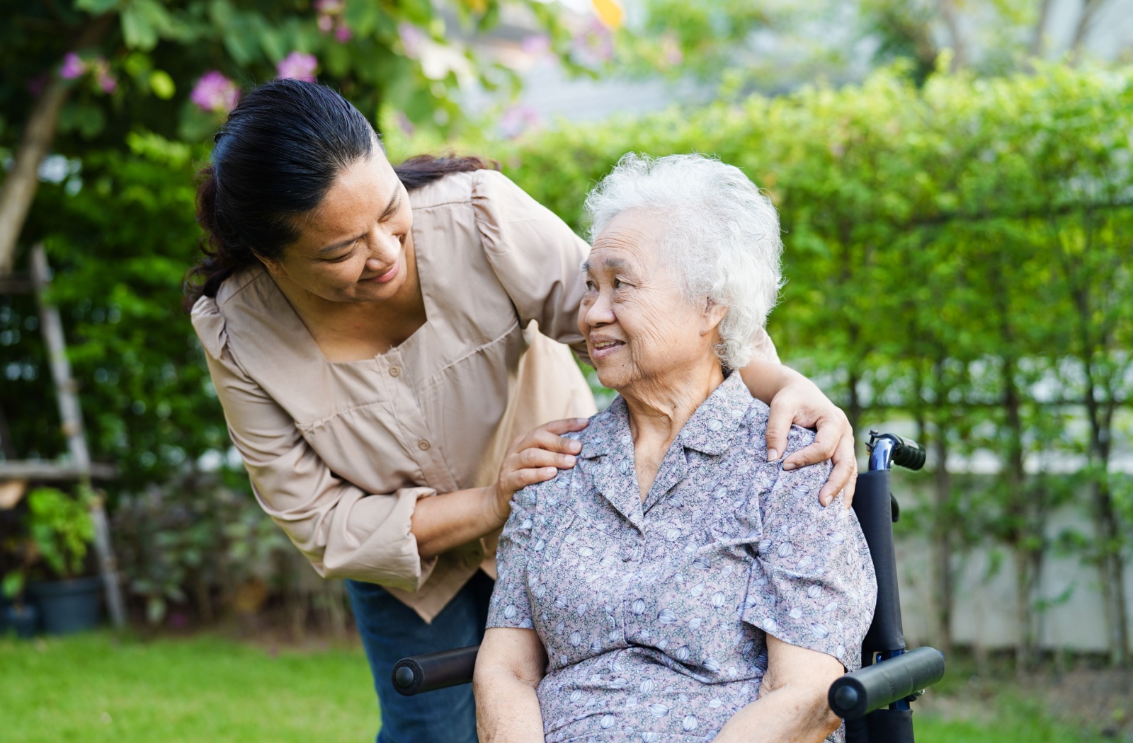 An adult child checks on their older parent while on a careful walk together in the gardens of a senior living community