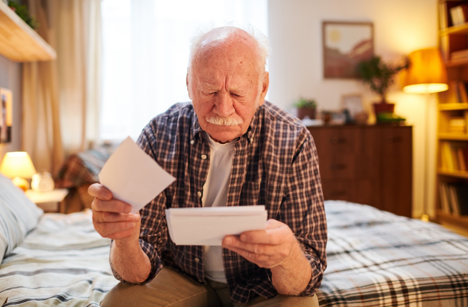 A senior looks concerned as they sit on their bed looking through a stack of photographs