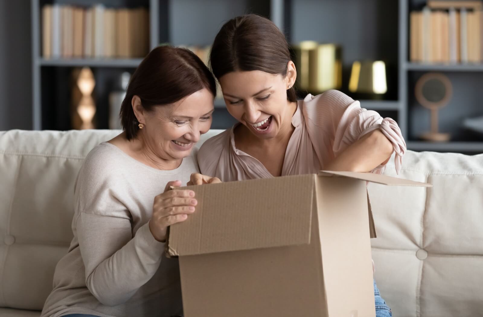 An older adult woman and a young woman happily unpacking a cardboard box together.