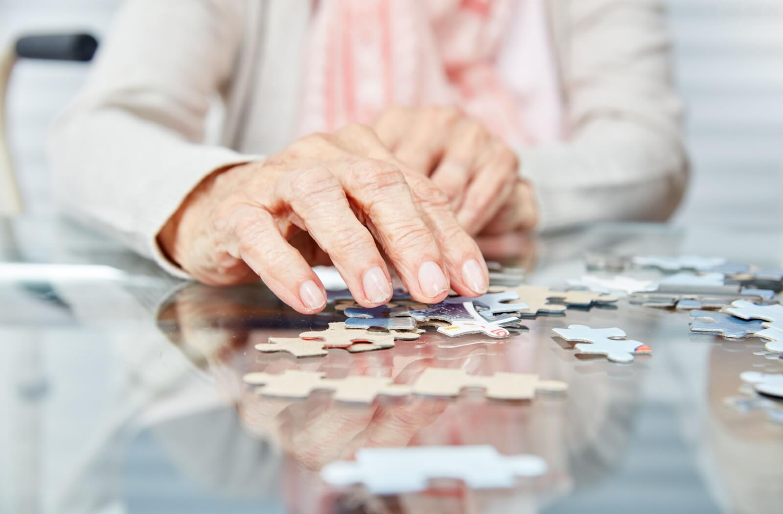 A close-up image of a senior's hands doing a puzzle as a means of maintaining good cognitive function.