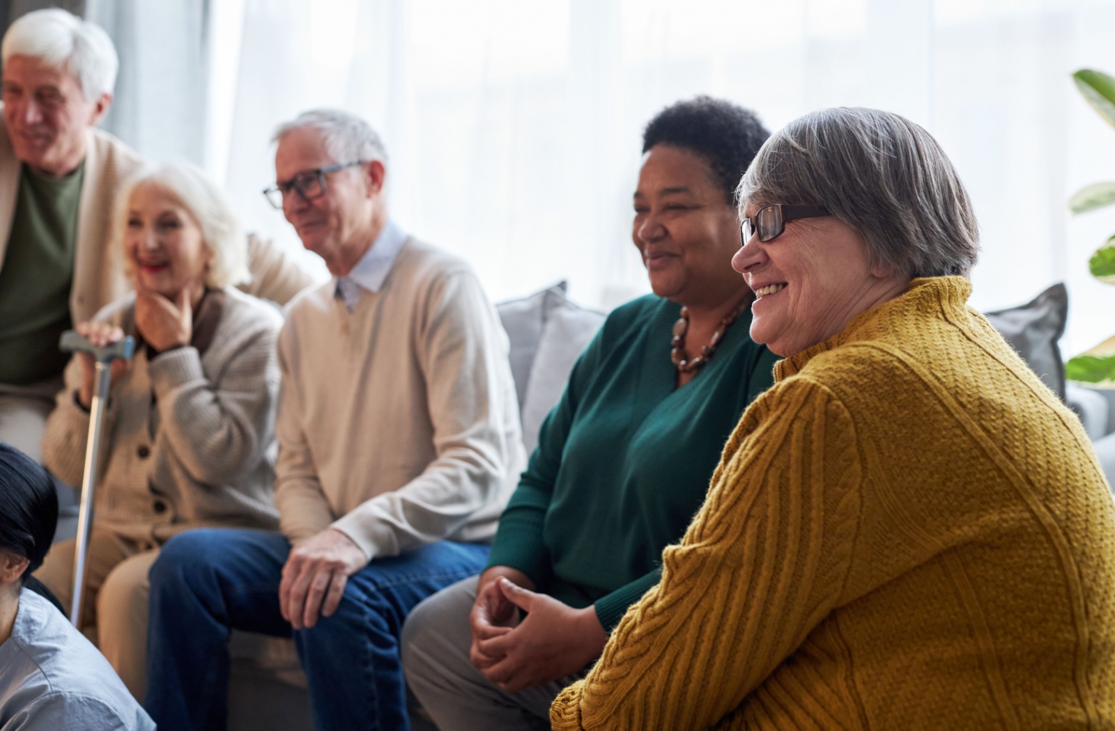 A group of seniors sits around and enjoys each other's company in their assisted living community.