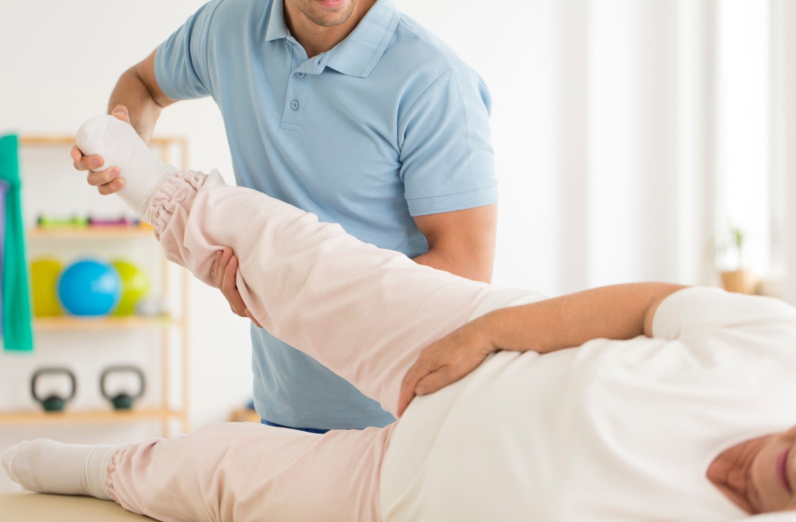 A physical therapist assists a senior with hip mobility exercises.
